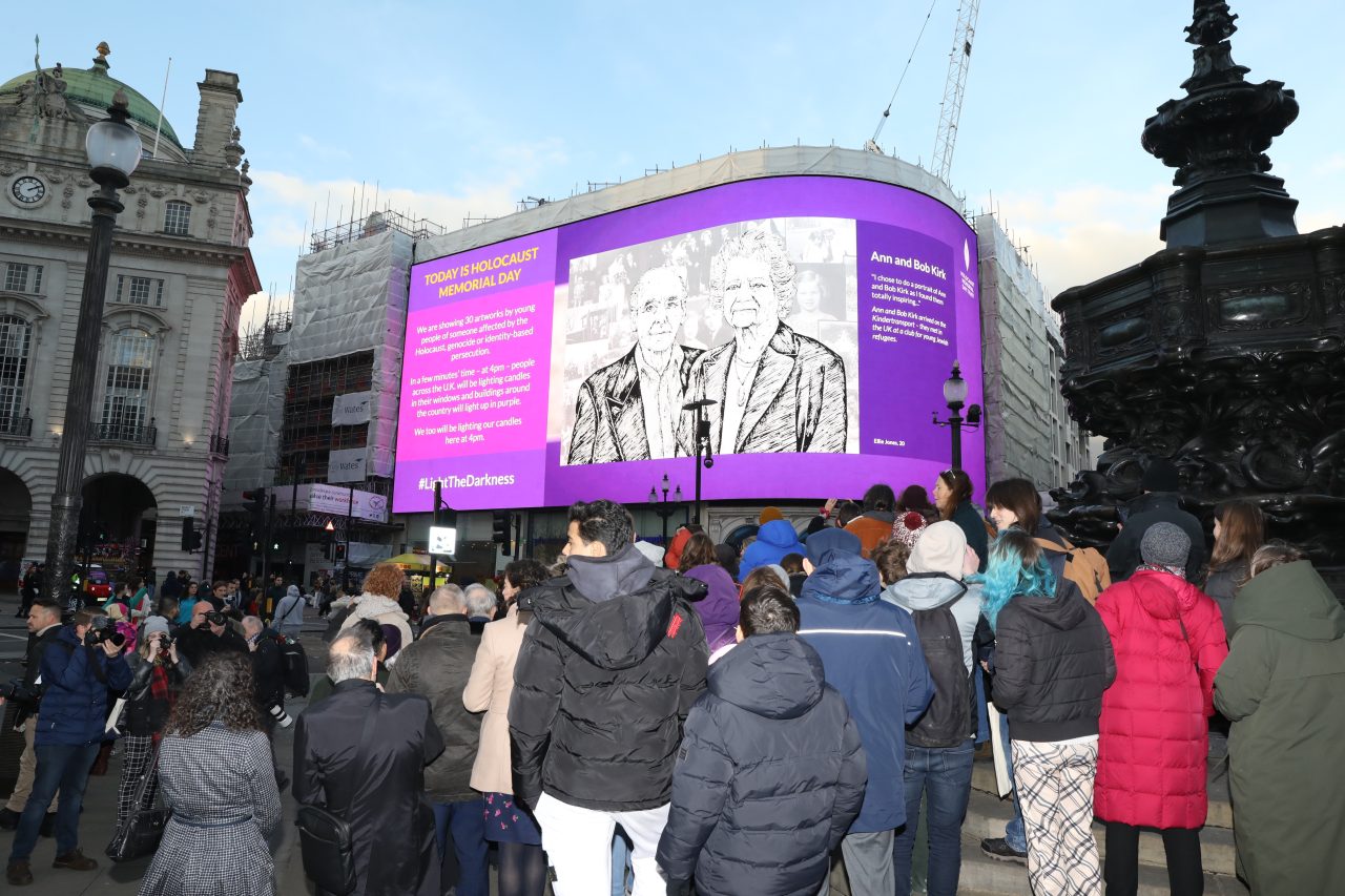 Crowds watch the portraits in Piccadilly Circus for the Light the Darkness national moment